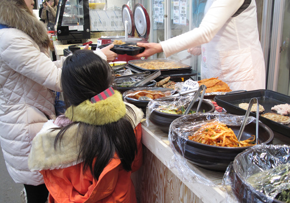 아이와 어머니가 엽전도시락에 반찬을 받고 있다.