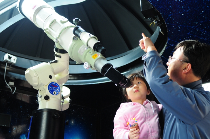 한 어린이가 과학관의 망원경으로 천체관측을 하며 흥미진진한 설명을 듣고 있다.